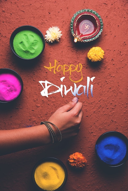 Kartka z życzeniami szczęśliwego diwali kliknięta przy użyciu elementów festiwalu Diwali, takich jak kolorowe rangoli w miskach, gliniana lampa diwali lub diya i dziewczyna lub dziewczyna robiąca rangoli, pisząca szczęśliwe diwali