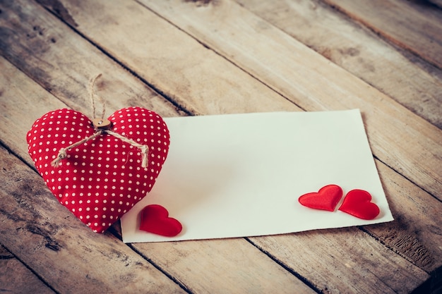 Zdjęcie kartkę z życzeniami i czerwone serce z miejsca na tekst na drewnianym tle