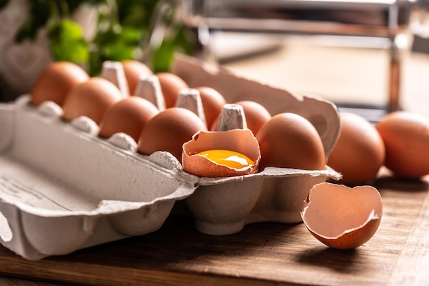 Kartonowe pudełko pełne świeżych jaj kurzych z żółtkiem w rozbitym jajku na kuchennym blacie.