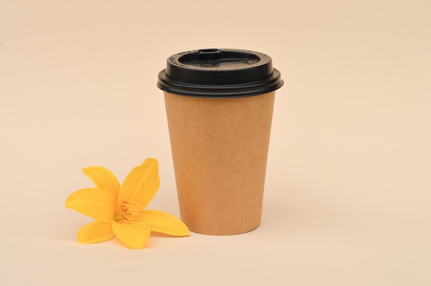 Kartonowy kubek na kawę odpowiedni do ponownego użycia obok żółtego kwiatu lilii na beżowym tle zero odpadów ostrożne podejście do natury