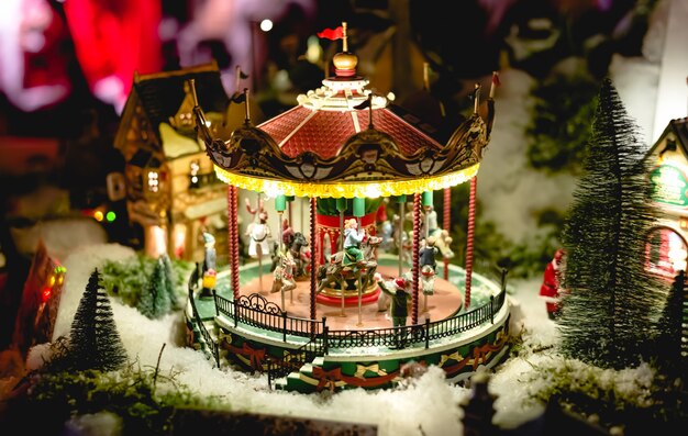 Karuzela w miniaturowej zabawce European Christmas Fair. Zimowa scena wigilijna z tradycyjnymi miniaturowymi domami wiejskimi. Vintage miasto nocną zabawkę z karuzelą.