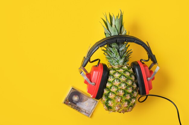 Kaseta i ananas w czerwonych słuchawkach retro na żółtym tle, widok z góry