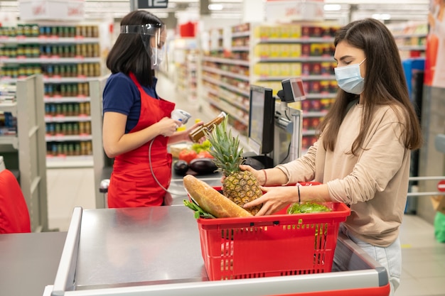 Kasjer supermarketu i klient przestrzegający zasad ochrony osobistej podczas dni kwarantanny koronawirusa, noszący maski