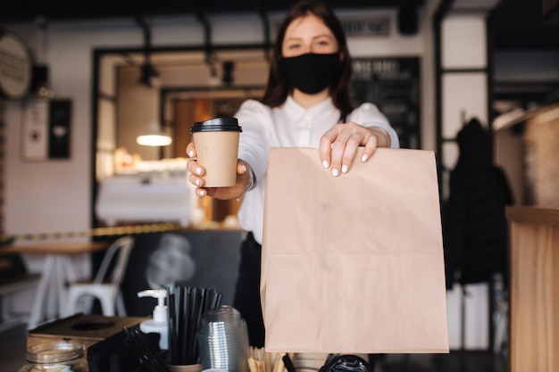 Kasjerka z maską na twarz serwująca kawę do sklepu klienta otwarta po zamknięciu kobieta trzyma pakiet