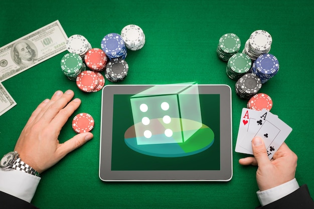 kasyno, hazard online, koncepcja technologii i ludzi - zbliżenie gracza w pokera z kartami do gry, komputerem typu tablet i żetonami przy zielonym stole w kasynie