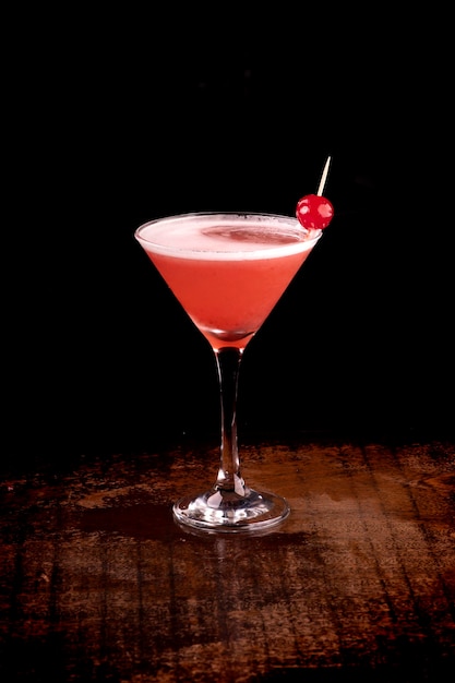 Kąt widzenia kieliszka koktajlowego truskawkowego martini z wiśniowym i piankowym ciemnym tłem na drewnianym stole