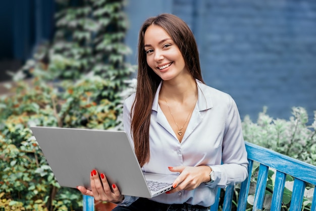 Kaukaska brunetka administratorka restauracji stojącej i pracującej na zewnątrz na laptopie