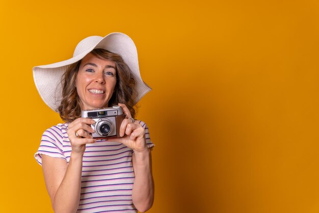 Kaukaska dziewczyna w koncepcji turystycznej z aparatem fotograficznym w dłoni i ciesząca się letnimi wakacjami na żółtym tle