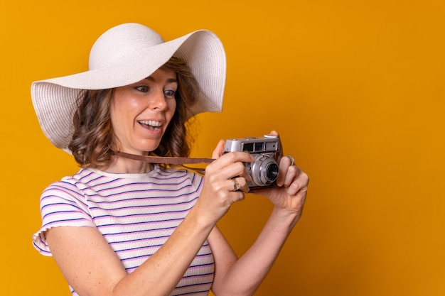 Kaukaska dziewczyna w koncepcji turystycznej z kapeluszem i aparatem fotograficznym, ciesząca się wakacyjnym żółtym tłem