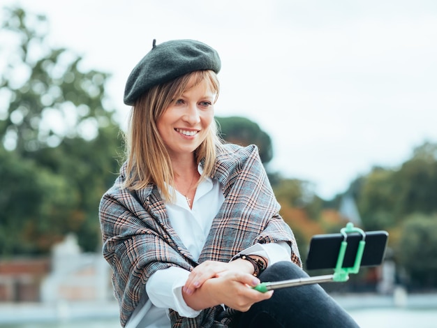 Kaukaska dziewczyna z francuskim kapeluszem robi sobie zdjęcia kijem do selfie