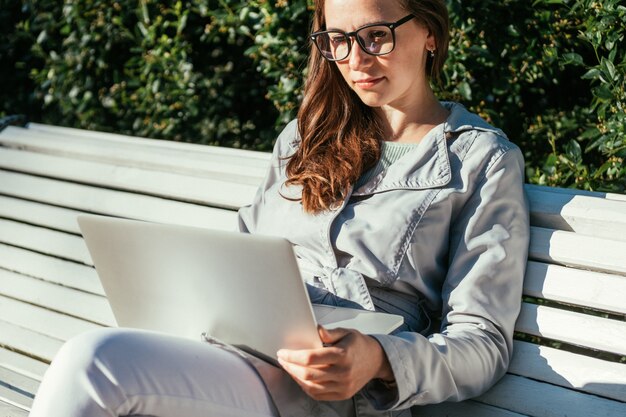 Kaukaska freelancer dziewczyny obsiadanie w parku na ławce i działanie na laptopie w lecie