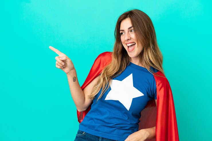 Zdjęcie kaukaska kobieta super hero odizolowana na niebieskim tle, wskazując palcem w bok i prezentująca produkt