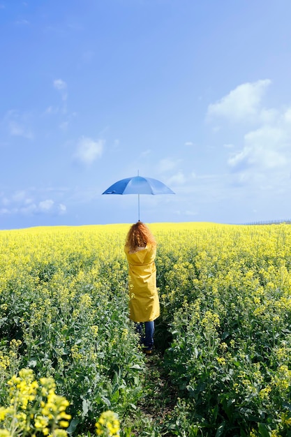 Kaukaska kobieta trzyma parasol w pięknym żółtym polu w deszczowy letni dzień