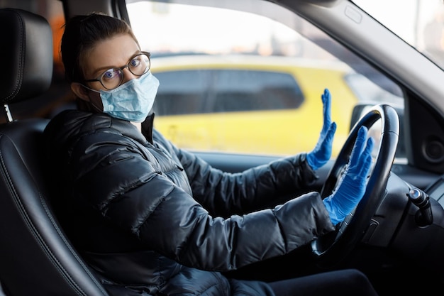 Kaukaska kobieta w okularach antywirusowa maska medyczna i niebieskie lateksowe rękawiczki siedząca w samochodzie