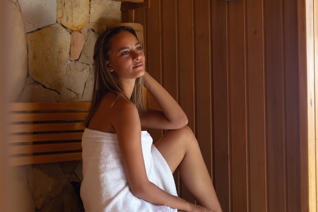 Kaukaska młoda kobieta w szlafroku relaksująca się w saunie. Koncepcja spa, wellness i relaksu