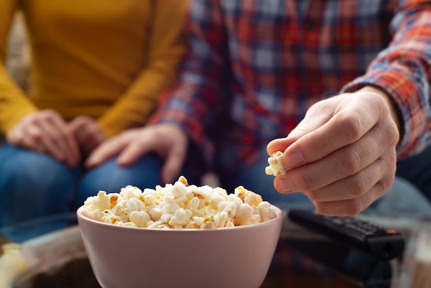 Kaukaska para siedzi na kanapie z popcornem i pilotem do telewizora