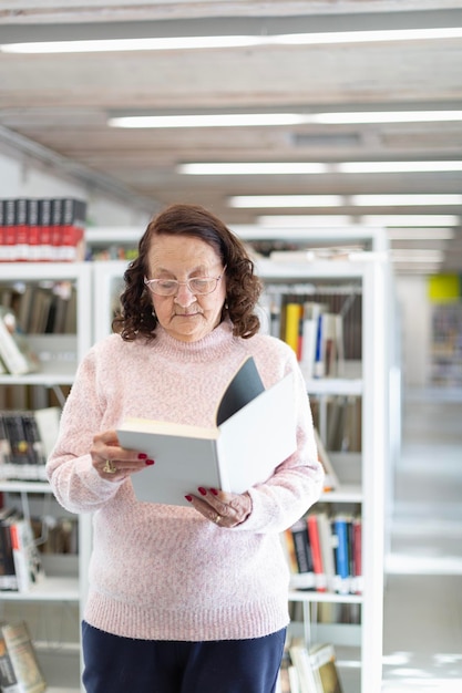 Zdjęcie kaukaska starsza kobieta czytająca książkę w bibliotece publicznej