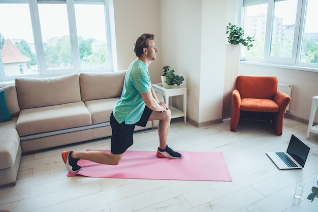 Kaukaski blondyn w odzieży sportowej używa laptopa w domu podczas cyfrowych lekcji fitness