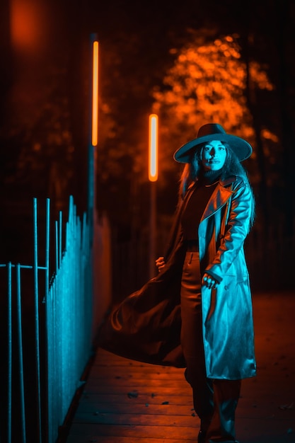 Kaukaski brunetka dziewczyna z kapeluszem w nocy w parku oświetlonym niebieskim światłem. Zimowa moda i styl życia w nocy