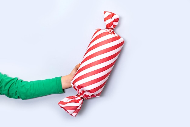 Kaukaski dzieciak dziecko ręka trzyma kształt pudełka cukierków na jasnym tle skopiuj miejsce na projekt lub tekst transparent makieta świąteczny nowy rok szablon