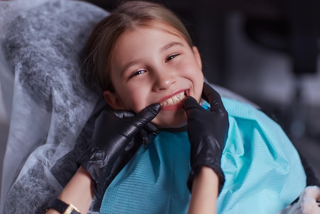 Kaukaski dziecko dziewczynka siedzi w fotelu medycznym, podczas gdy dentysta dopasowuje zęby w klinice dentystycznej za pomocą instrumentów dentystycznych narzędzi, szczegół zdjęcie twarzy. profesjonalny lekarz specjalista.