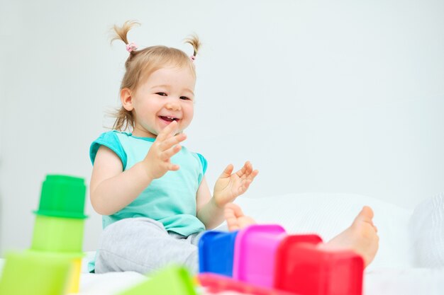 Kaukaski dziecko uśmiecha się i klaszcząc w dłonie, grając w kolorowe zabawki