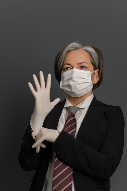 Kaukaski kobieta w masce ochronnej założyć rękawiczki jednorazowe. Dojrzała kobieta urzędnik przed pracą zakłada sprzęt ochronny. Koncepcja wybuchu koronawirusa