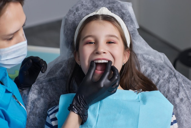 Kaukaski małe dziecko dziewczynka niewidoczny aligner i wskazujący na jej idealne proste zęby. Koncepcja opieki stomatologicznej i zaufania.