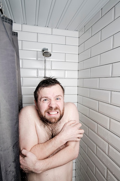 Kaukaski mężczyzna jest niezadowolony z faktu, że musi umyć się pod zimnym prysznicem, który zamarł