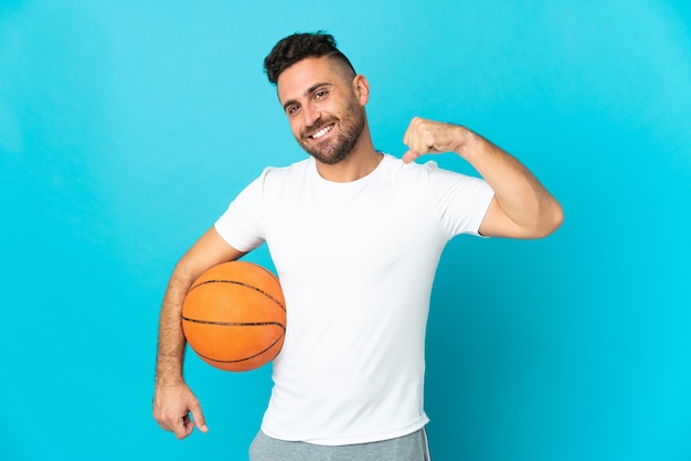 Kaukaski mężczyzna na białym tle na niebieskim tle gra w koszykówkę i jest z siebie dumny