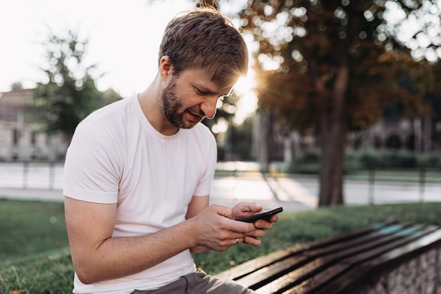 Kaukaski mężczyzna siedzący na ławce i używający smartfona