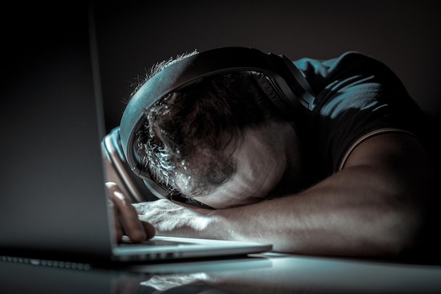 Kaukaski mężczyzna śpiący na swoim laptopie ciężko pracujący pracownik biurowy biorący krótką przerwę na sen przepracowany wyczerpany wolny strzelec