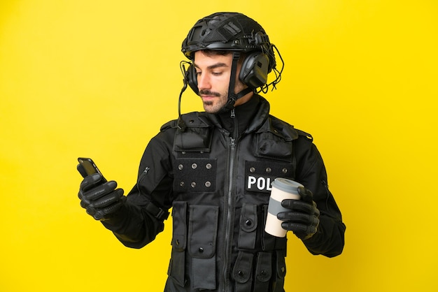 Kaukaski mężczyzna SWAT na żółtym tle trzyma kawę na wynos i telefon komórkowy