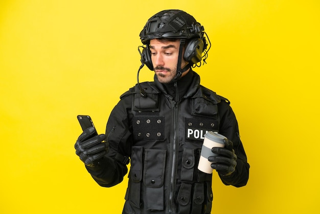 Kaukaski mężczyzna SWAT na żółtym tle trzymający kawę na wynos i telefon komórkowy, myśląc o czymś