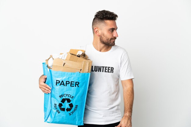 Kaukaski mężczyzna trzyma torbę do recyklingu pełną papieru do recyklingu na białym tle patrząc w bok