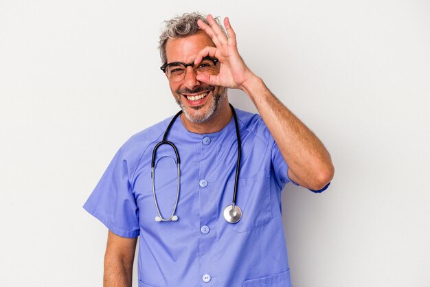 Kaukaski mężczyzna w średnim wieku pielęgniarka na białym tle podekscytowany, zachowując ok gest na oku
