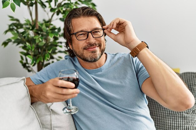 Kaukaski mężczyzna w średnim wieku uśmiechający się pewnie do picia wina w domu
