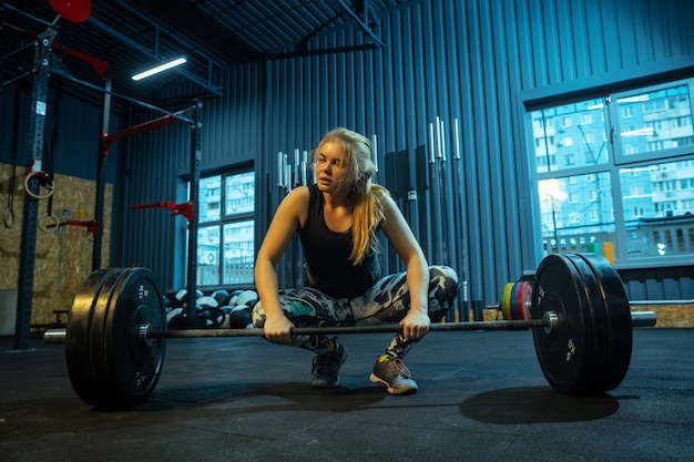 Kaukaski nastolatka praktykujących w podnoszeniu ciężarów w siłowni. Trening ze sztangą modelka sportowa, wygląda na skoncentrowaną i pewną siebie. Koncepcja budowy ciała, zdrowego stylu życia, ruchu i działania.