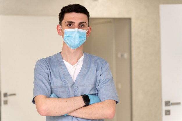 Kaukaski Przystojny Młody Mężczyzna Profesjonalny Lekarz Nosi Maskę Ochronną Na Twarzy Stojąc W Szpitalu I Patrząc W Kamerę. Koncepcja Opieki Zdrowotnej