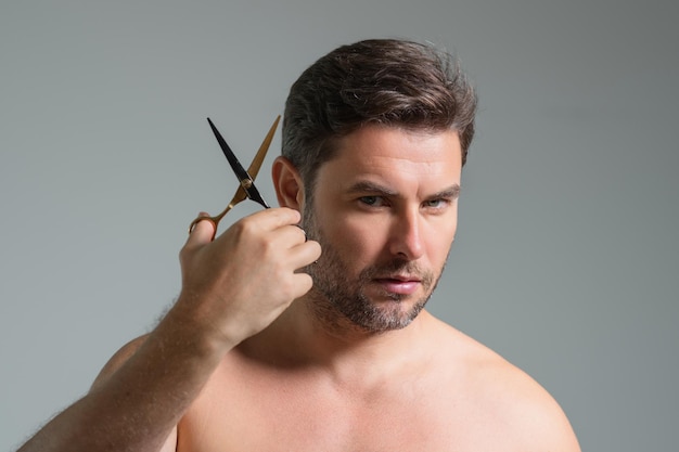 Kaukaski przystojny, pewny siebie mężczyzna próbuje sam obciąć włosy nożyczkami męski pasek do strzyżenia