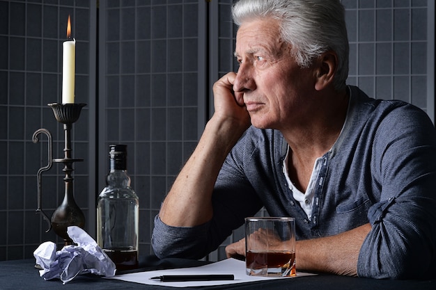 Kaukaski starszy mężczyzna z butelką alkoholu siedzi w pokoju