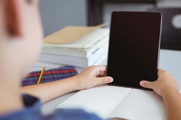 Kaukaski uczeń w klasie siedzi przy biurku za pomocą tabletu, z miejsca kopiowania na ekranie