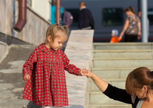 Zdjęcie kaukaskie dziecko w wieku dwóch lat trzymające matkę za rękę, czekające na wsparcie, aby zejść na dół