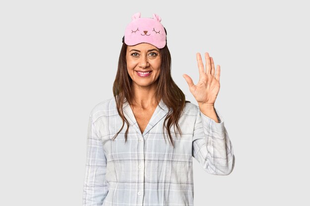 Zdjęcie kaukazka w średnim wieku w piżamie i masce w studiu uśmiechająca się wesoła pokazująca numer pięć