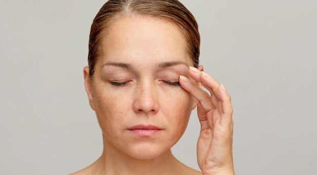 Zdjęcie kaukazka w średnim wieku z zamkniętymi oczami trzymająca palec na powieku, aby pokazać starzejące się oczy