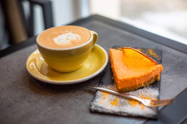 Zdjęcie kawa cappucino w żółtej filiżance z sernikiem w kawiarni