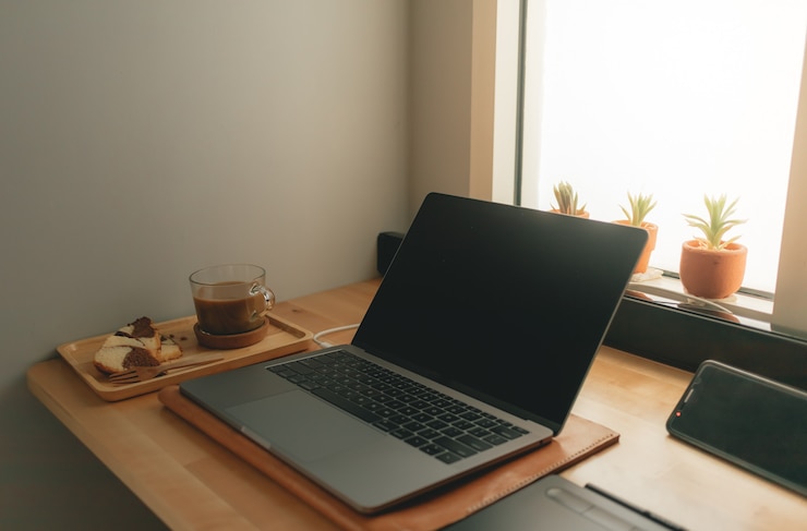 Zdjęcie kawa i laptop na biurku w ciepłym świetle.