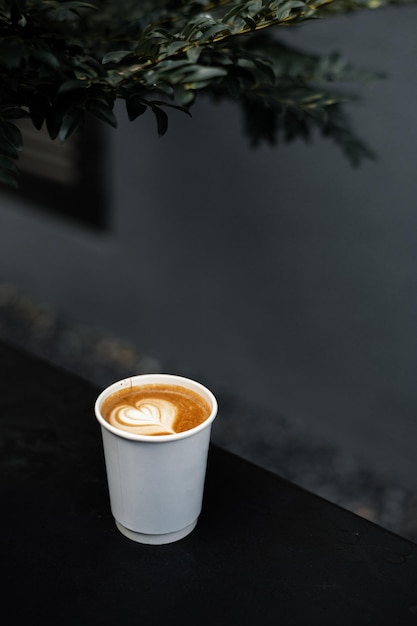 Kawa latte na papierowym kubku podana na białym stole w kawiarni