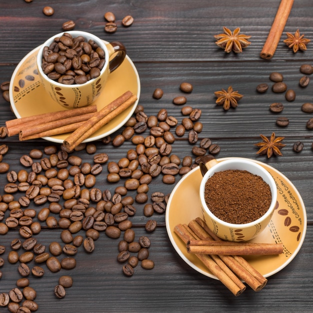 Zdjęcie kawa mielona i palone ziarna kawy w filiżankach. laski cynamonu na spodku. ziarna kawy i anyż gwiazdkowaty na stole. ciemne tło drewna. płaskie ułożenie