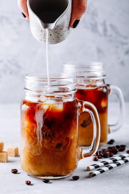 Kawa mrożona w szklanych słoikach z masonem z mlekiem i kostkami lodu na szarym tle